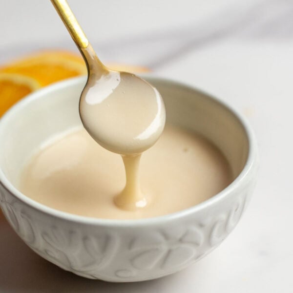 Orange icing in a bowl with a spoon dipped in it.