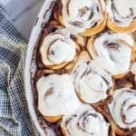 twelve sourdough cinnamon rolls covered in cream cheese icing in a baking dish.