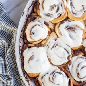 twelve sourdough cinnamon rolls covered in cream cheese icing in a baking dish.