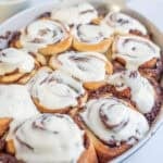 a casserole dish filled with cream cheese frosted cinnamon rolls.