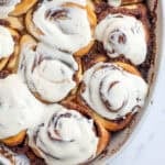 a casserole dish full of sourdough cinnamon rolls topped with a cream cheese glaze.