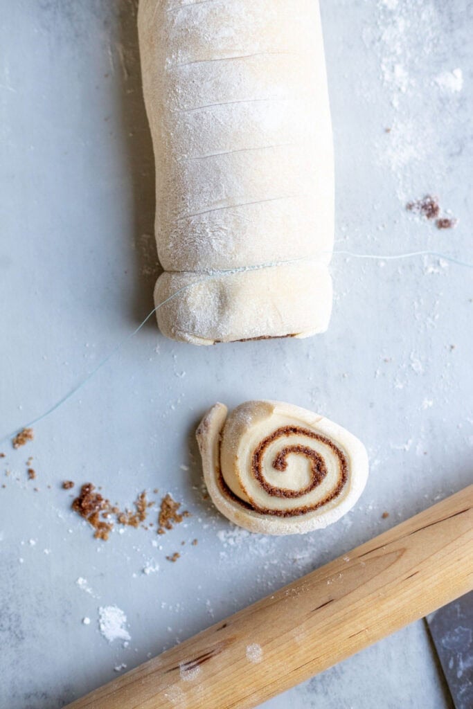 Cinnamon roll dough being cut into individual cinnamon rolls.