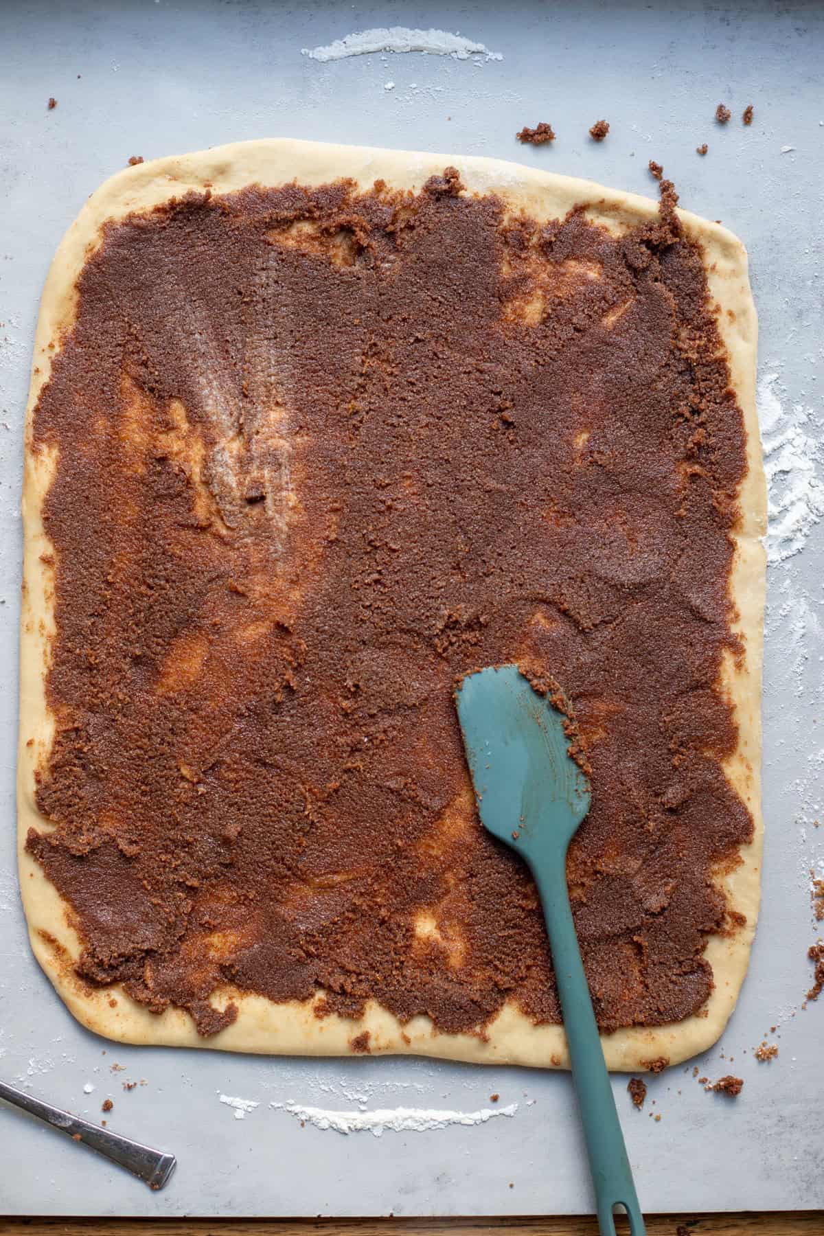 Cinnamon, butter, and sugar mixture spread evenly on the top of cinnamon roll dough.