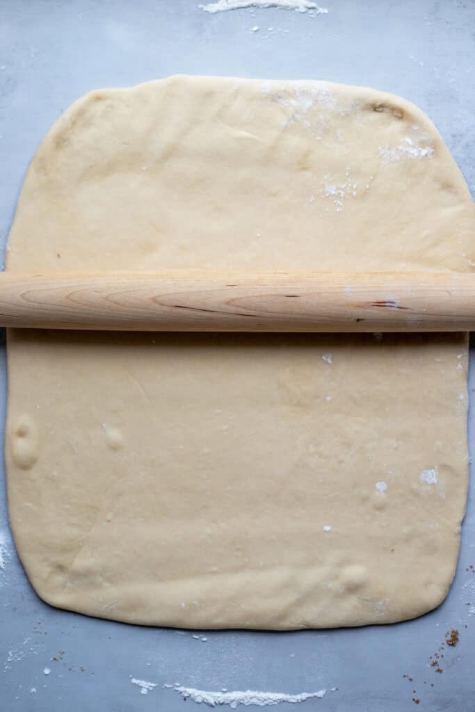 A ball of dough rolled out to a 12x15 rectangle with a rolling pin on the dough.