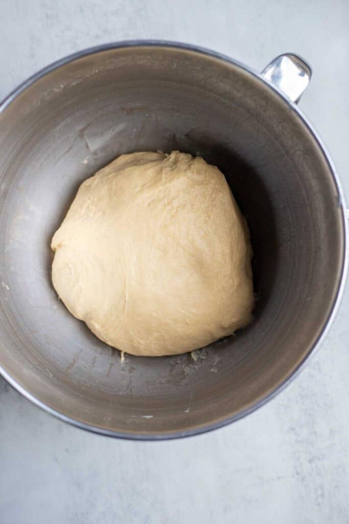 A kneaded ball of cinnamon roll dough in a stainless steel stand mixer bowl.