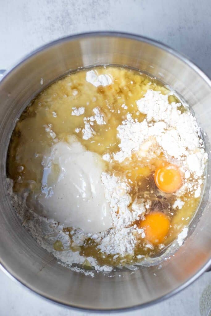 Flour, sourdough starter, oil, eggs, and vanilla in the stainless steel bowl of a stand mixer.