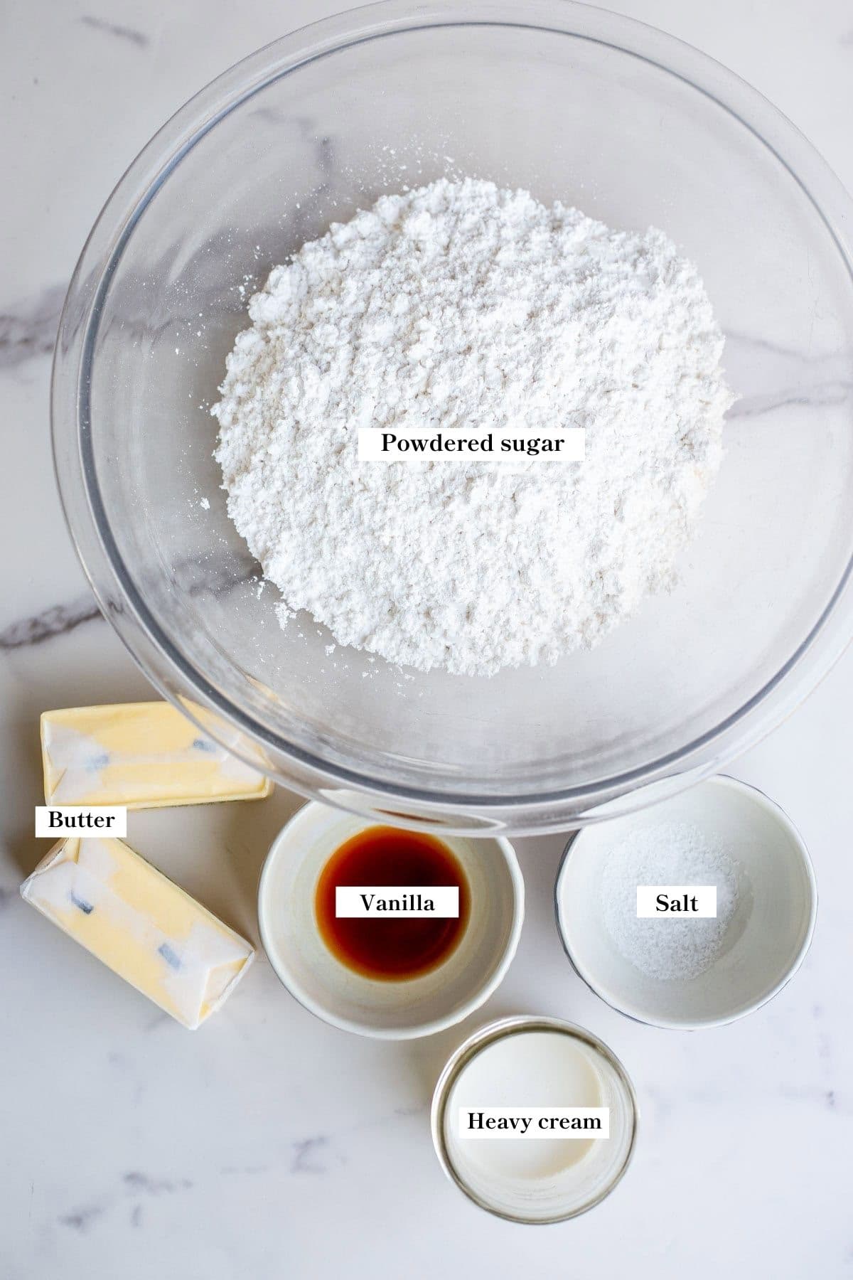 Powdered sugar, butter, vanilla, heavy cream, and salt on a marble counter.