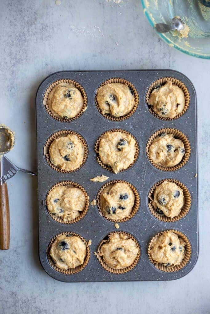 muffin batter scoops into a muffin pan.