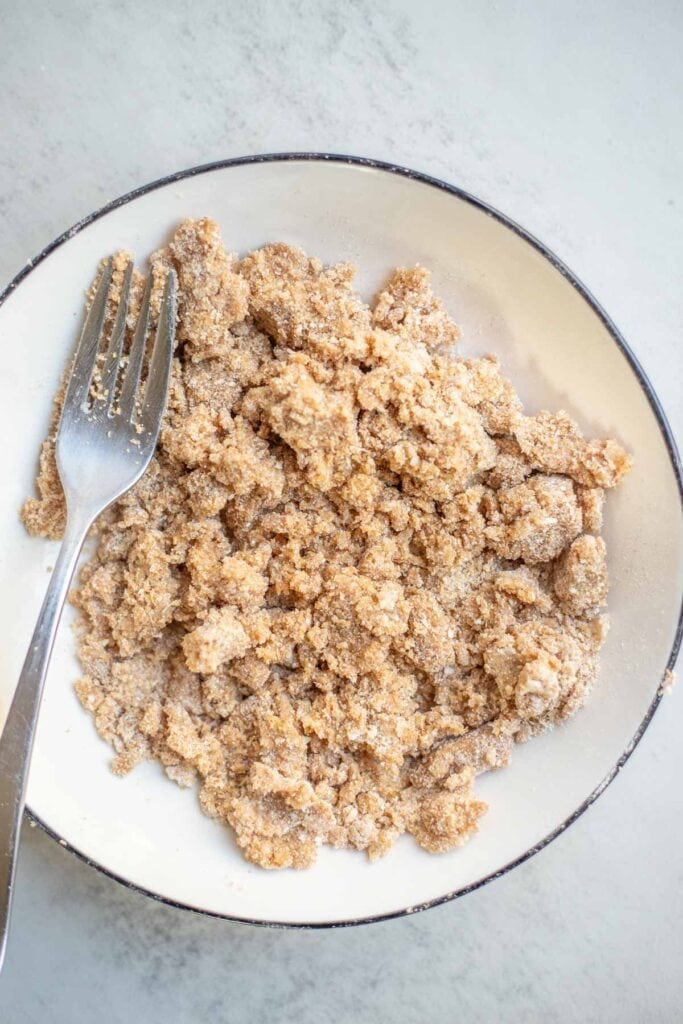 butter, flour, cinnamon, and sugar mixed together on a white plate to make a crumble.
