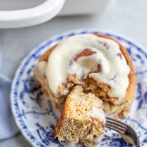 A cinnamon roll on a plate cut into with a fork.