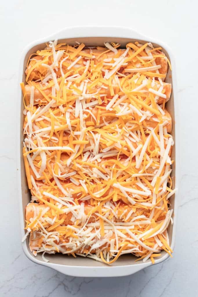 Cheese on top of enchiladas in a pan.