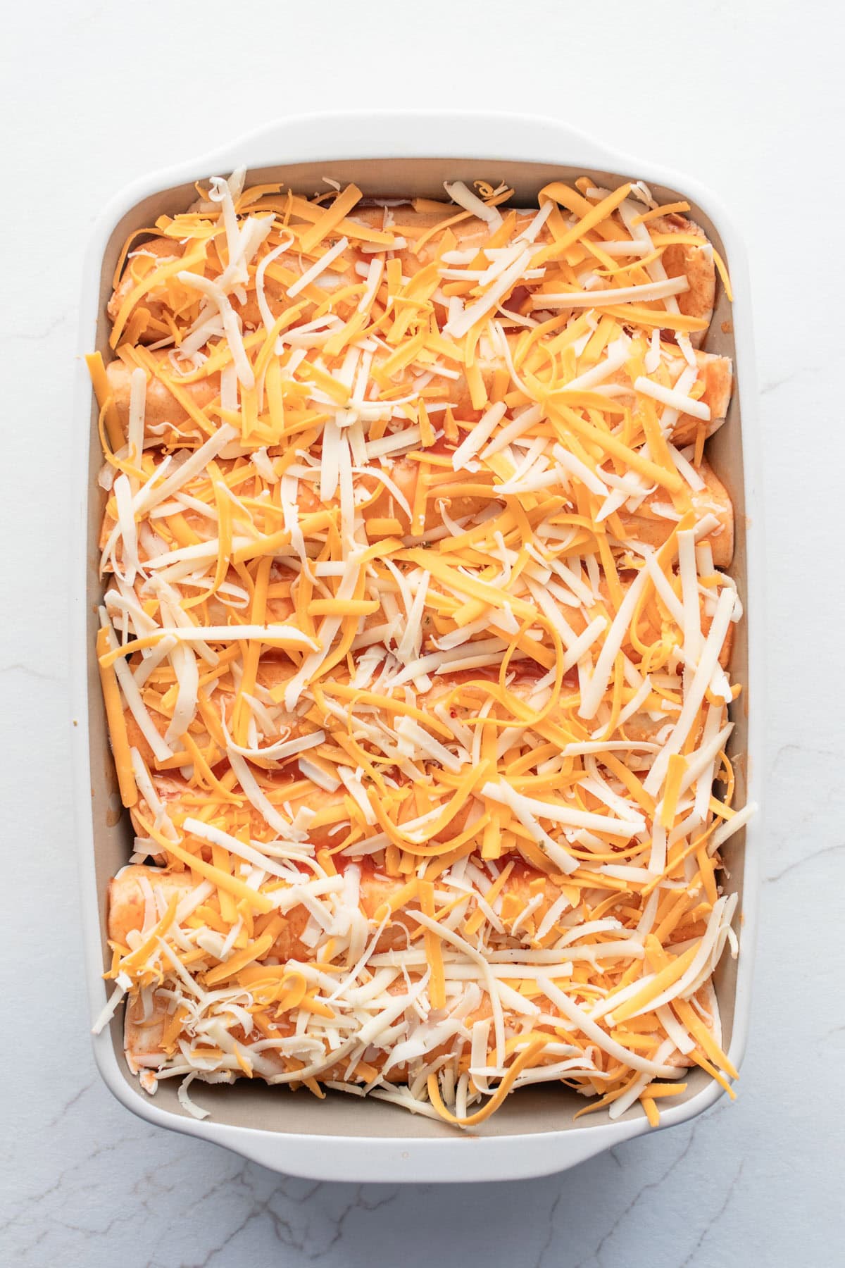 Cheese on top of enchiladas in a pan.