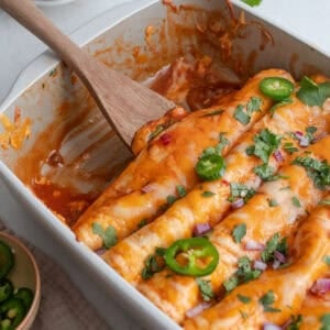 Enchiladas in a pan with a wooden spoon scooping them out.