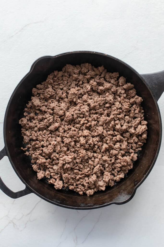 Beef browning in a cast iron skillet.