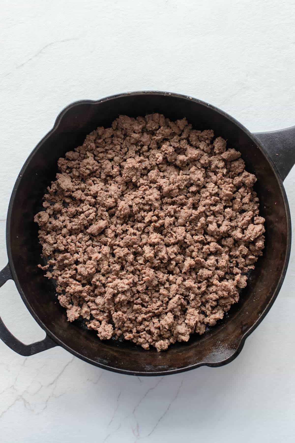 Beef browning in a cast iron skillet.