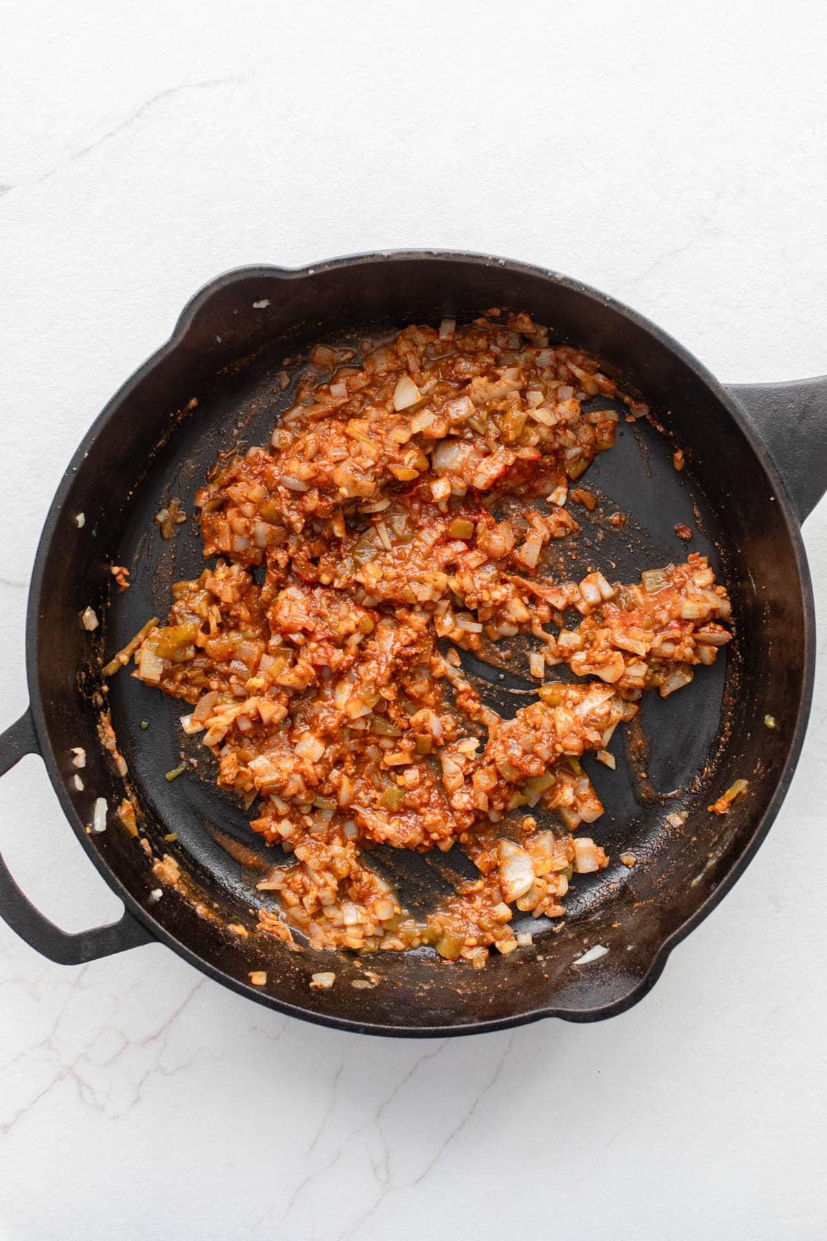 Tomato paste and seasoning mixed with onions in a cast iron skillet.