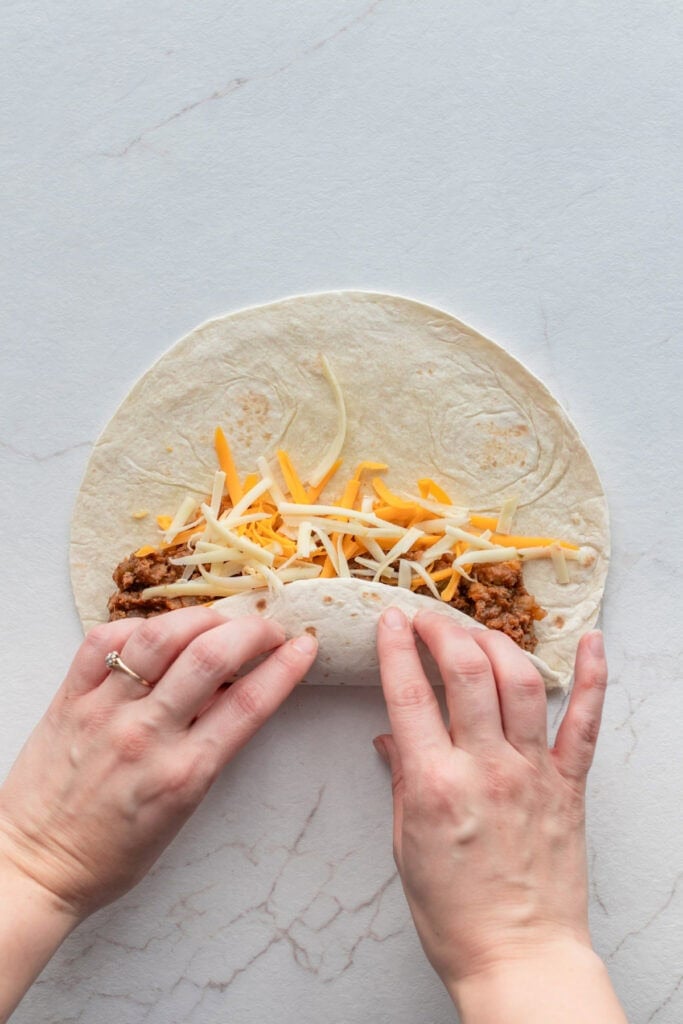 Hands rolling a tortilla filled with beef and cheese.