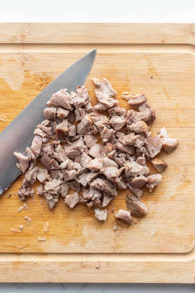 Chopped meat from ham hock on a cutting board with a knife.