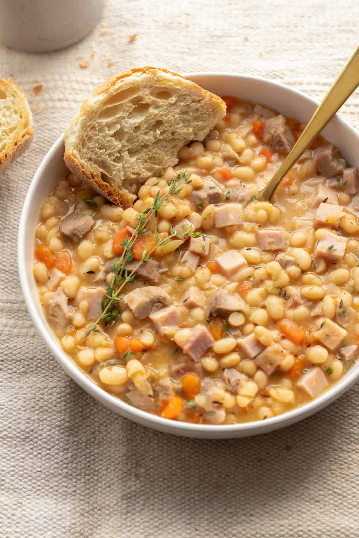 Ham and beans in a bowl with a slice of bread.