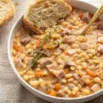 A bowl of ham and beans with bread.