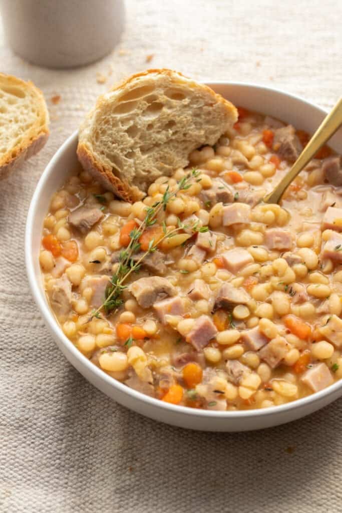 A bowl of ham and beans with bread.
