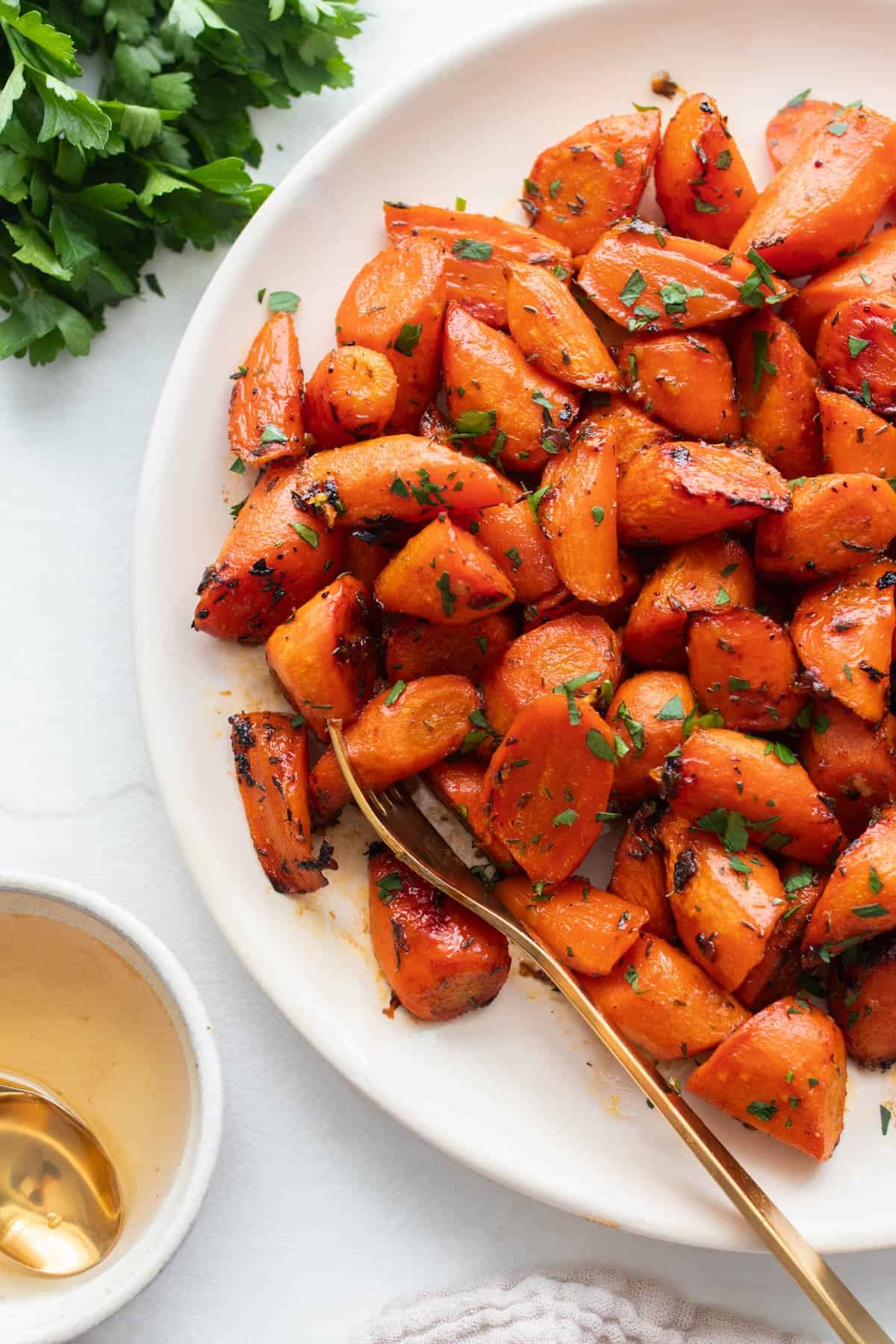 A plate of bite sized roasted carrots with a spoon.