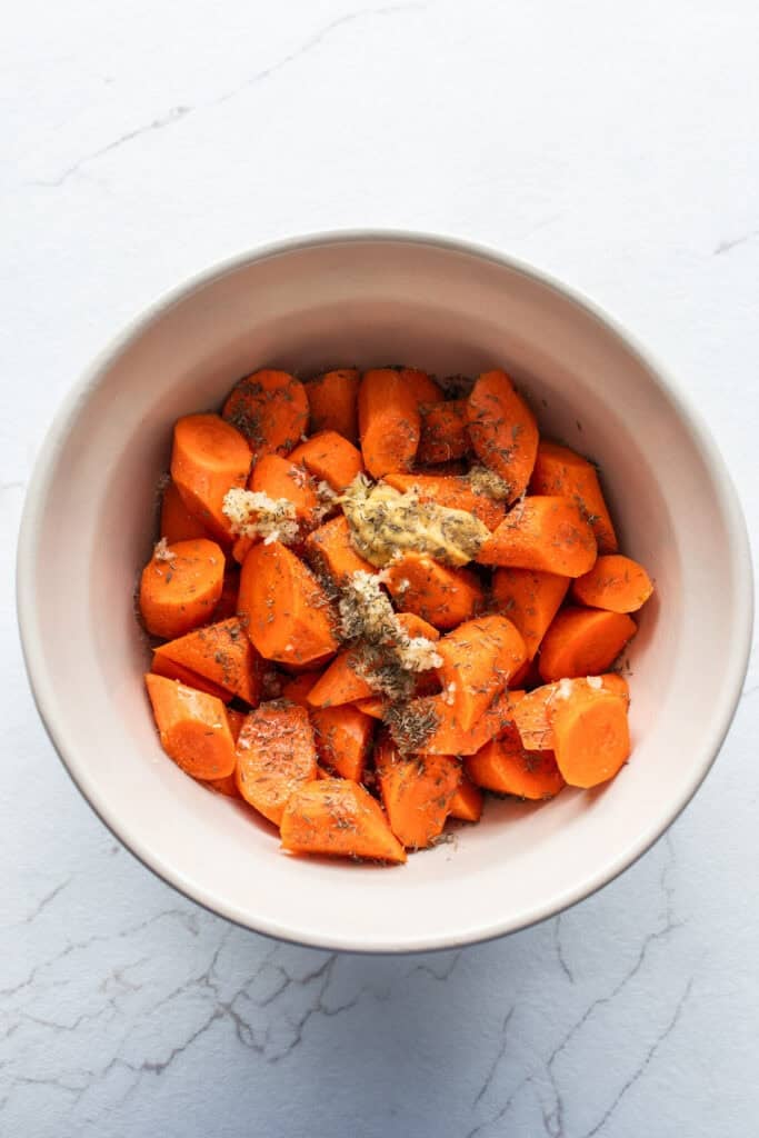 Bite sized carrots in bowl with seasonings and oil on top.