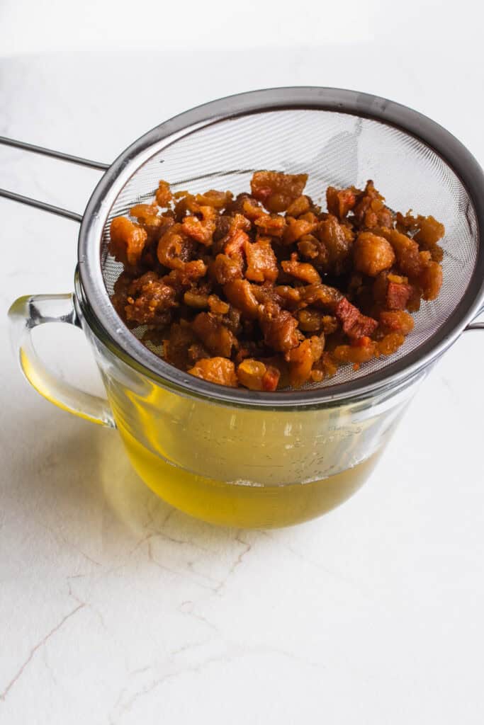 rendered pork fat being filtered through a fine mesh strainer.