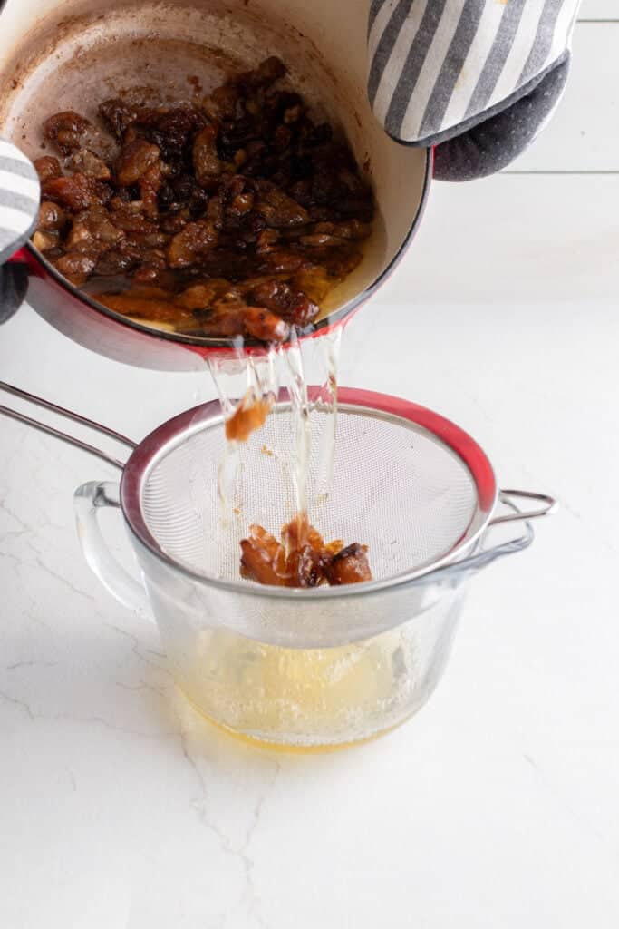 Someone pouring Dutch oven contents into a strainer over a glass container.