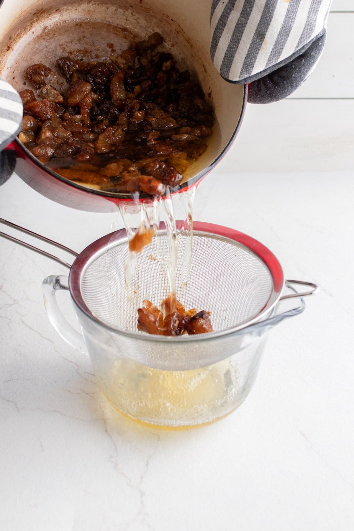 Someone pouring Dutch oven contents into a strainer over a glass container. 