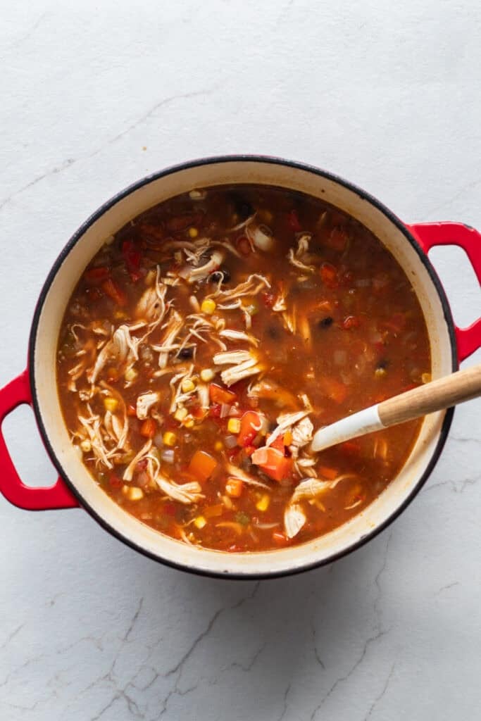 shredded chicken added to a dutch oven full of soup.