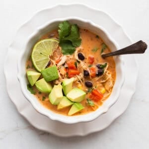 a bowl of southwest chicken soup topped with cheese, avocado, lime, and cilantro.