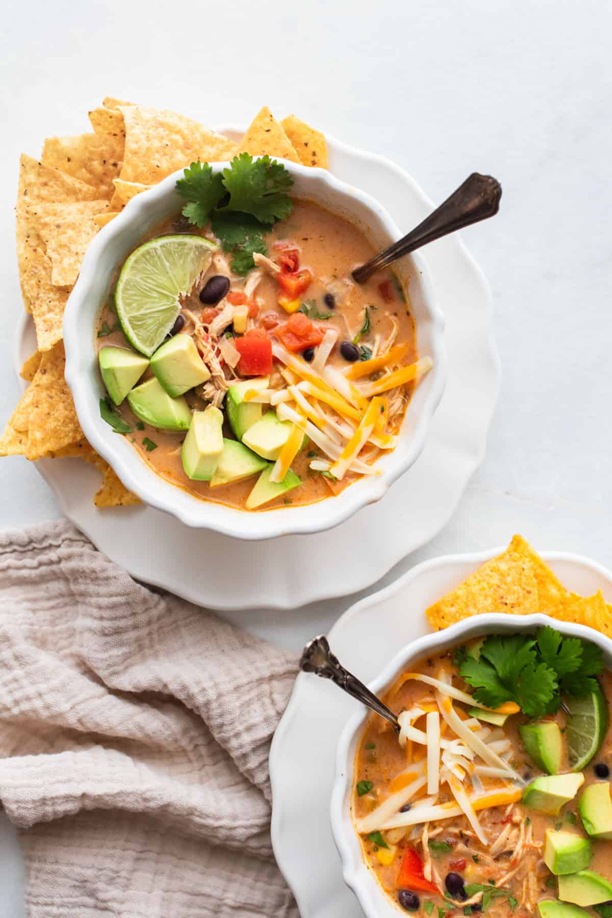 a bowl of chicken soup served with tortilla chips, lime, avocado, and cilantro.