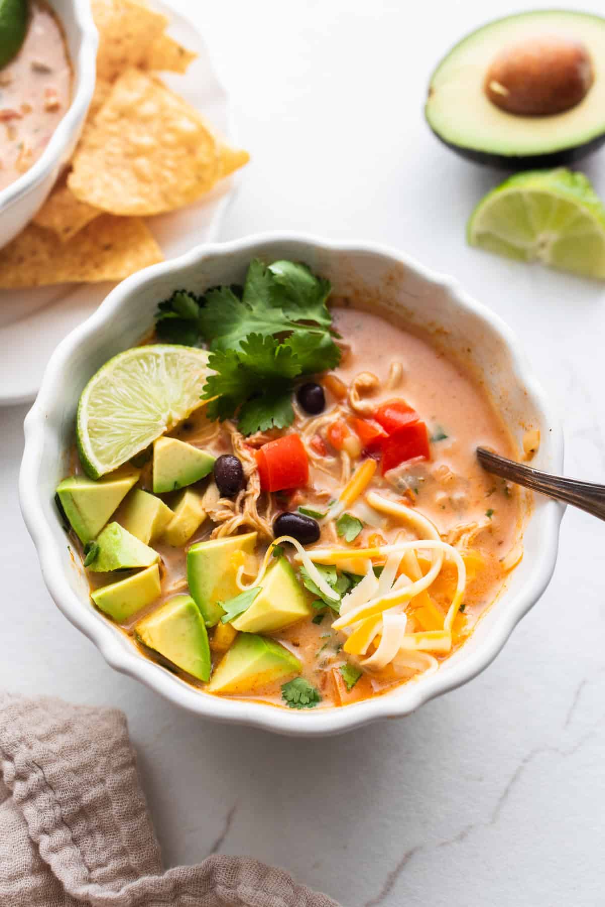 a white bowl full of southwest chicken soup topped with lime, avocado, and cheese.
