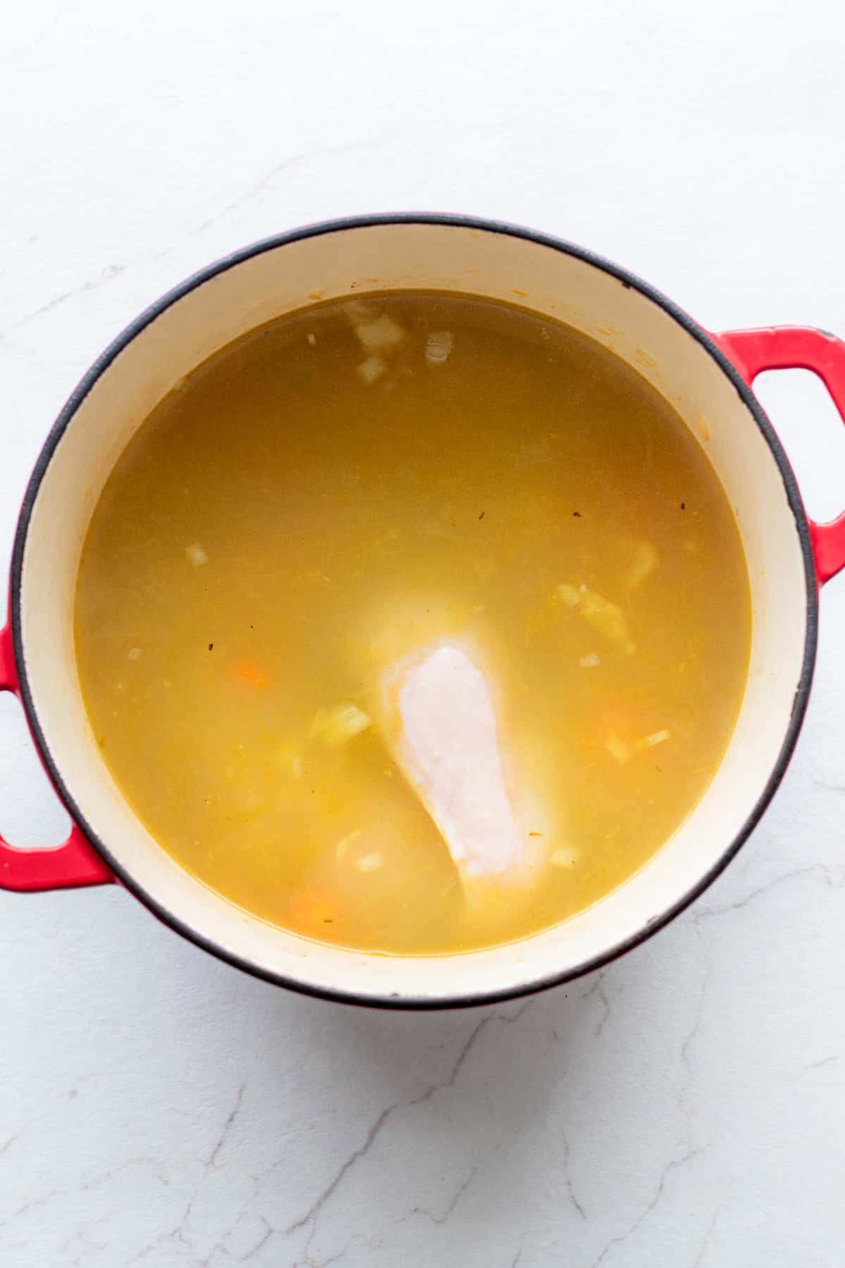 chicken broth and chicken breast added to a large dutch oven with onion and bell peppers.