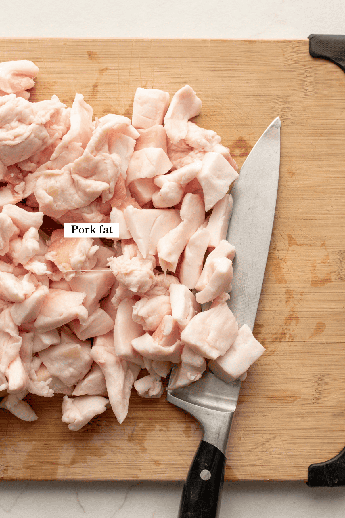 chopped pieces of pork fat on a wooden cutting board with a knife.