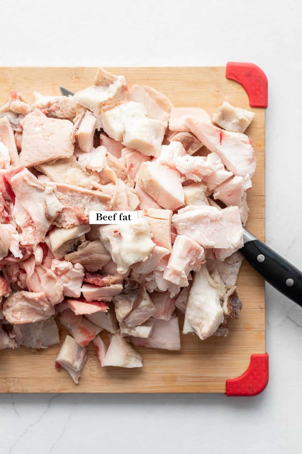 Beef fat cut into chunks on a wooden cutting board.