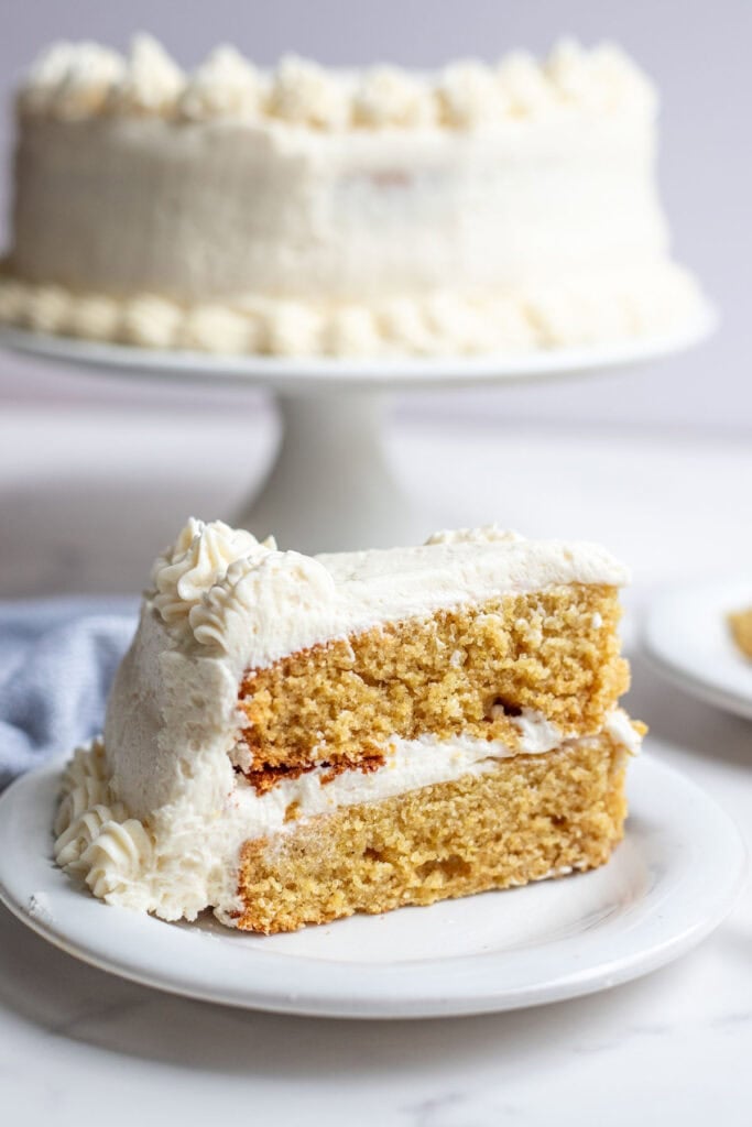 one slice of whole wheat cake with a vanilla buttercream frosting on a white dessert plate.