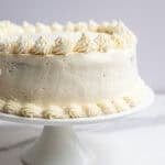 two round layers of cake stacked and iced with buttercream on a white cake plate.