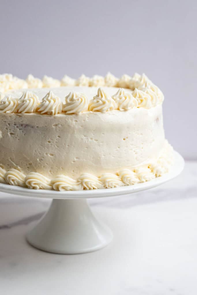 two round layers of cake stacked and iced with buttercream on a white cake plate.