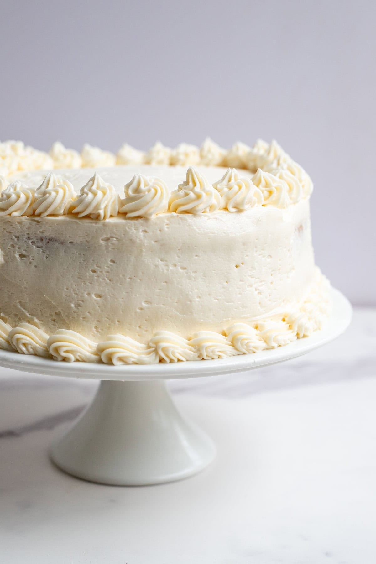 two round layers of cake stacked and iced with buttercream on a white cake plate.