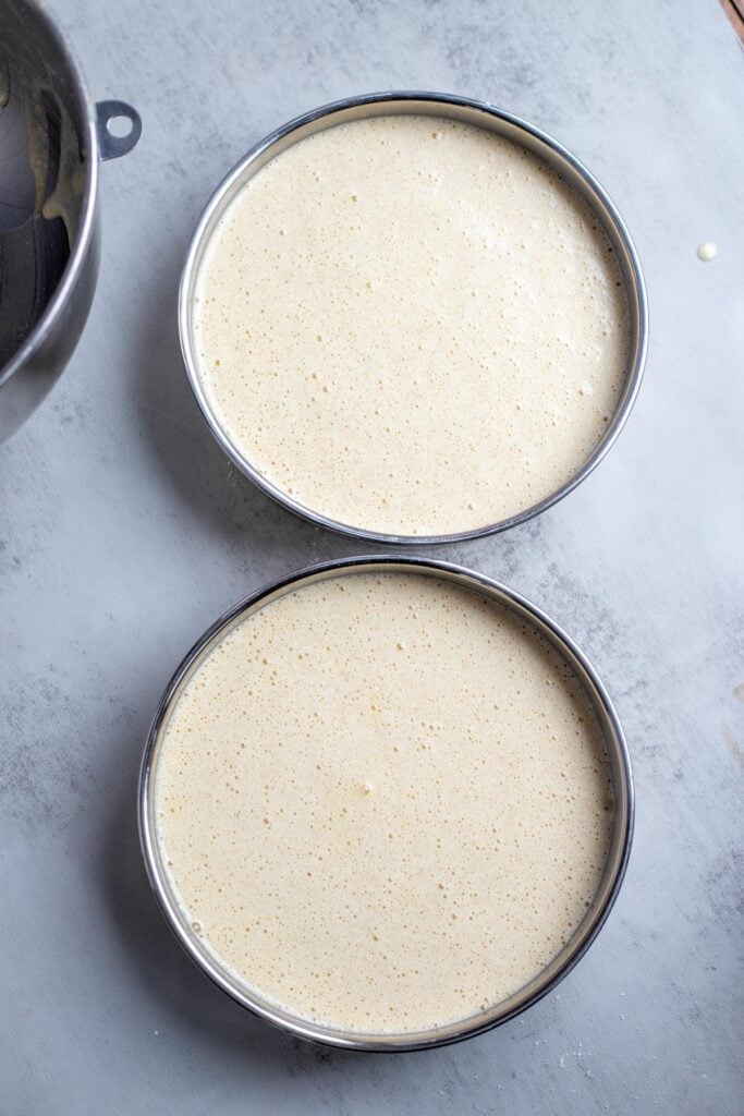 two 8" round cake pans filled with cake batter and sitting on the counter.