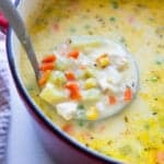A Dutch oven of chicken pot pie soup with a ladle scooping some out.