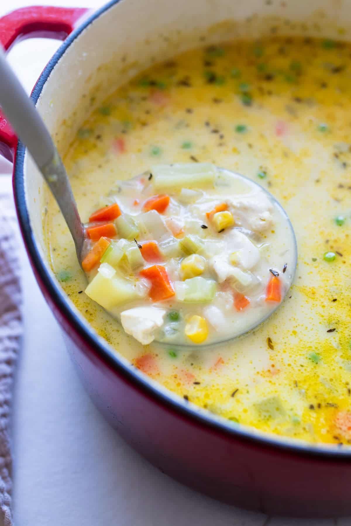 A Dutch oven of chicken pot pie soup with a ladle scooping some out.