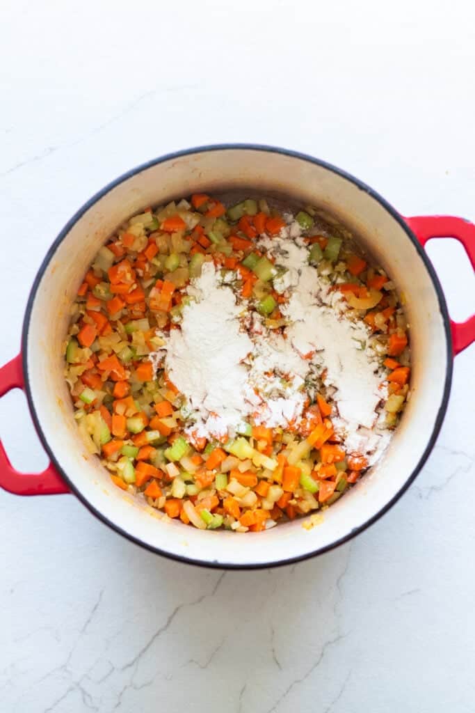 Flour sprinkled over celery and carrot pieces in a Dutch oven.