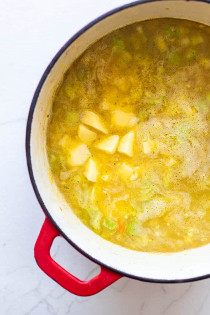 Broth and diced potatoes added to a Dutch oven full of chopped vegetables.