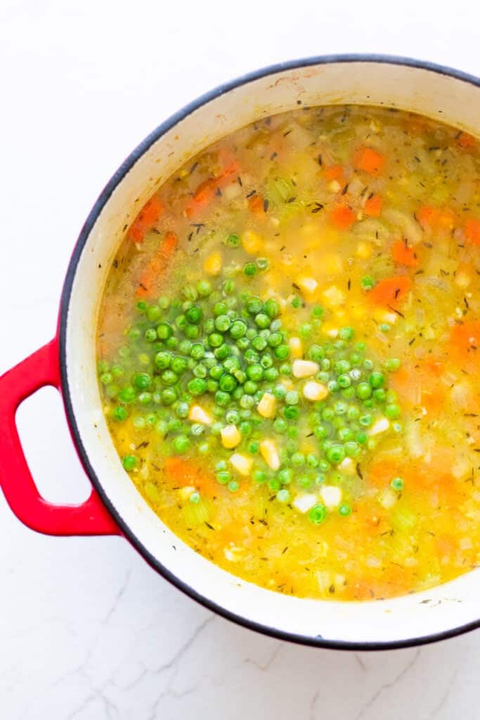 Peas and chicken added to a Dutch oven of vegetables and potatoes and broth.