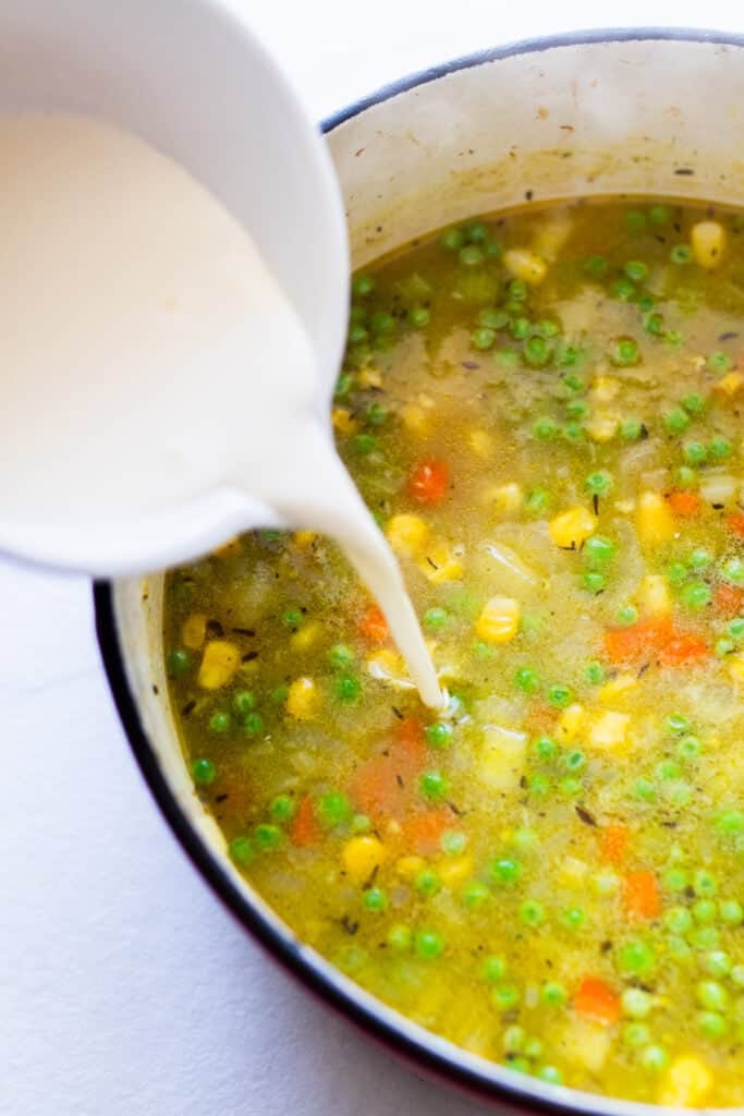 Heavy cream being poured into a Dutch oven full of soup.