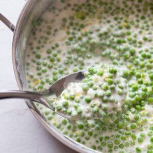 Cream peas in a sauce pan with a spoon scooping up some.