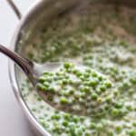 A spoon full of cream peas with a sauce pan of cream peas in the background.
